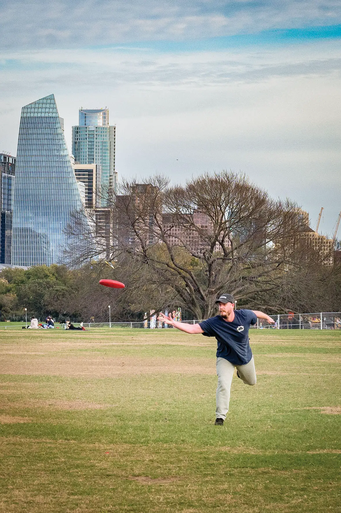 Man throwing a red disc in a disc golf game in Zilker Park