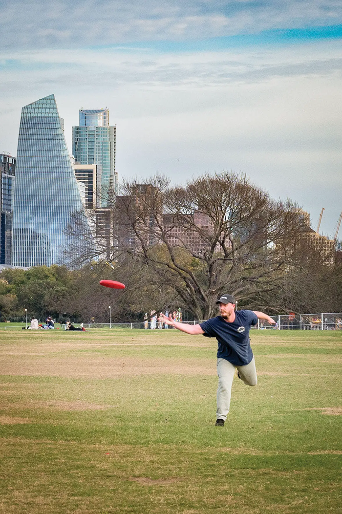 Man throwing a red disc in a disc golf game in Zilker Park