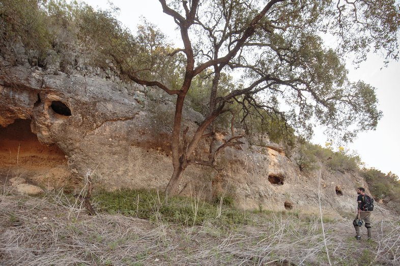 Man walking along the outside of a cave with multiple wholes along the outside of the cave.