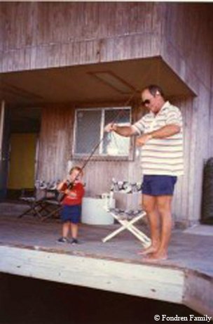Man and child setting up fishing pole on the front porch of a house