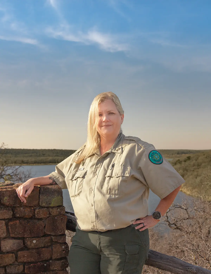 Nikki Elms complex superintendent at Lake Mineral Wells Sate Park standing outside at a lake overlook with had resting on a wall