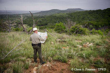 Park Planner looking at a map in a grassy area and a view of the mountains