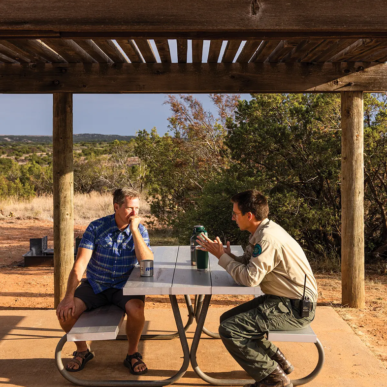 Park Ranger speaking with a man at a picnic table under a pavilion
