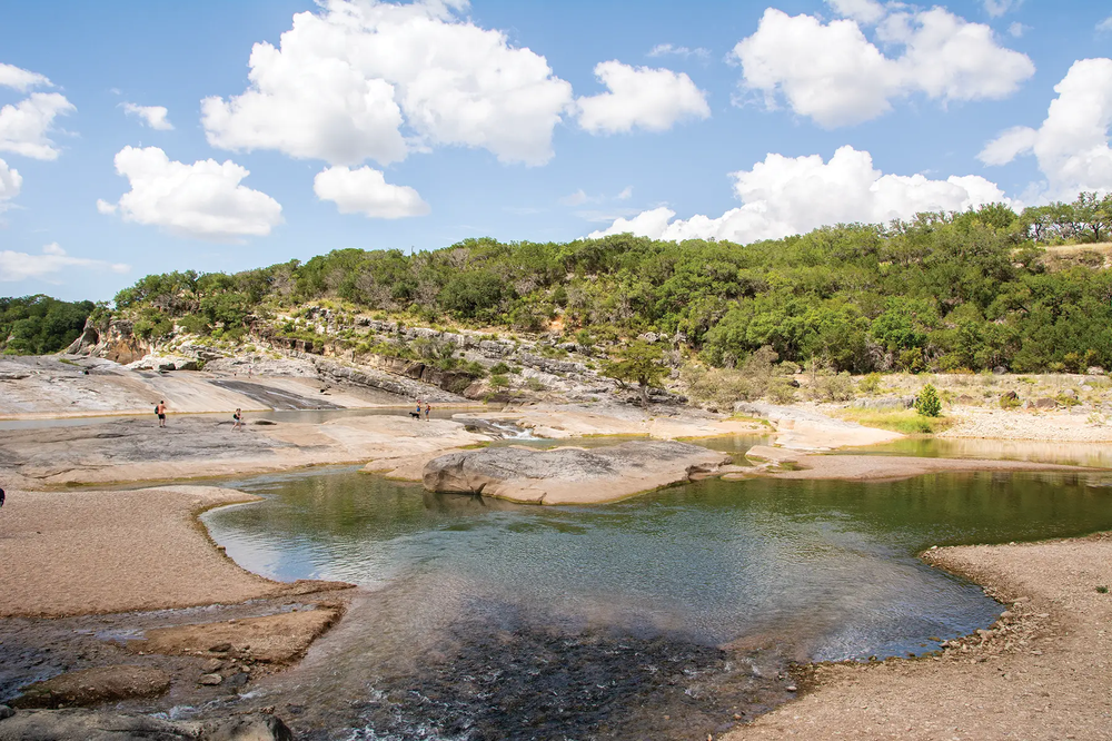 Pedernales Falls with a mostly dry river bed with some watery areas swimmers in the distance
