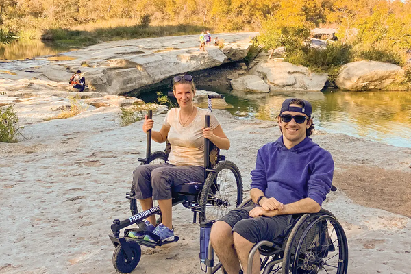 People in all terrain wheelchairs on a rocky trail by water
