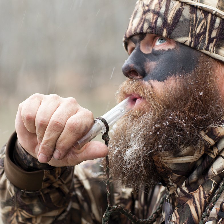 Person in camouflage using a duck call.