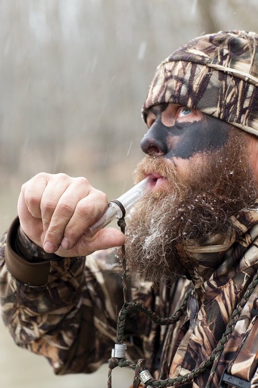 Person in camouflage using a duck call.