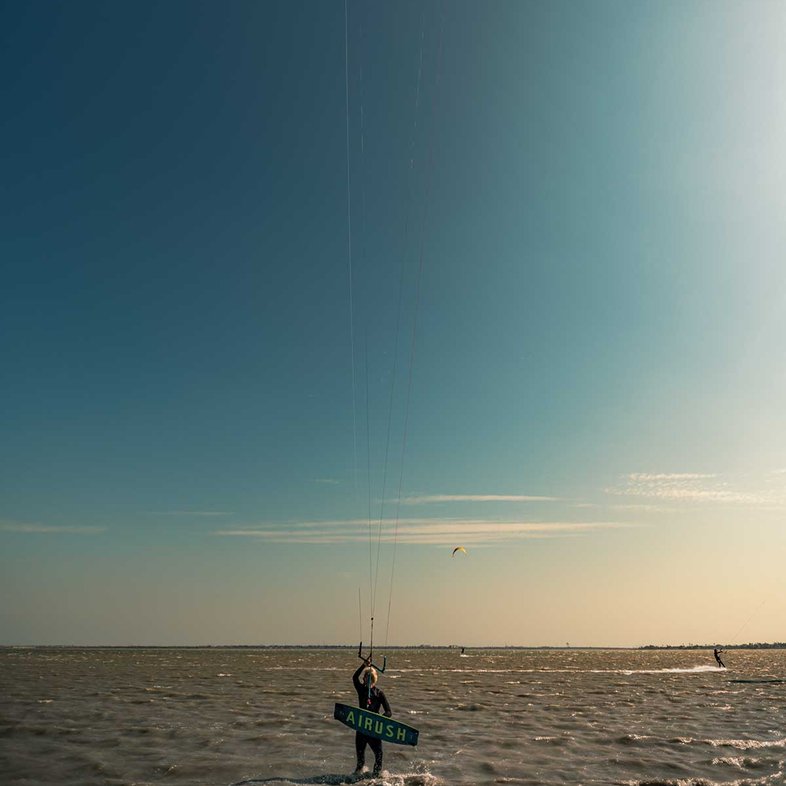 Person walking into the water with a kiteboard.