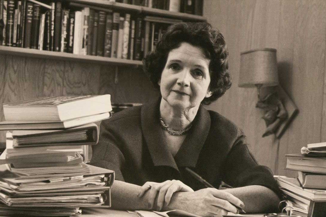Rachel Carson sitting at a desk in her book filled office.
