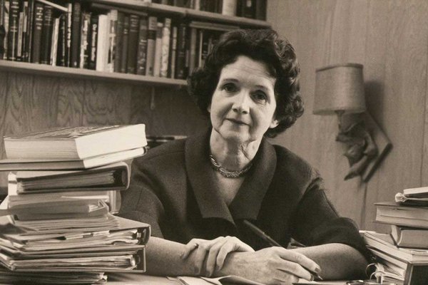 Rachel Carson sitting at a desk in her book filled office.