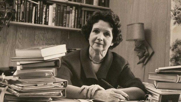 Rachel Carson sitting at a desk in her book filled office.