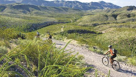 Mountain biker in red trailing behind other bikers with hills in the background
