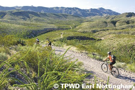 Mountain biker in red trailing behind other bikers with hills in the background
