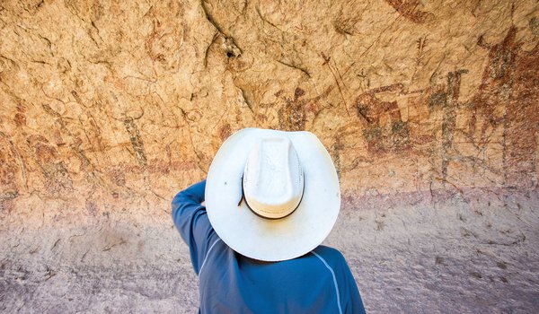 Person in blue shirt with a white hat looking at the canyon wall pictographs at the Lower Pecos Canyonlands