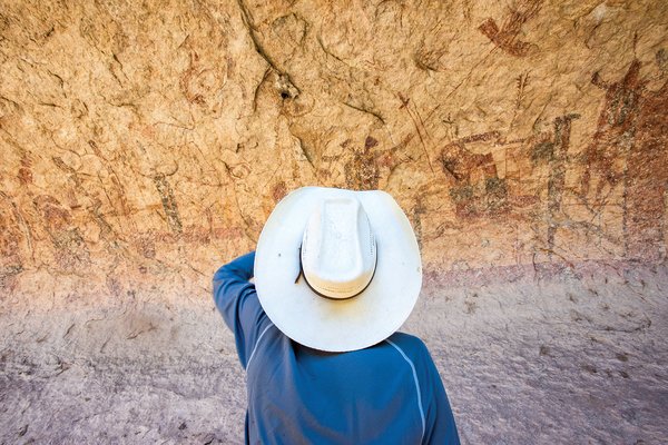 Person in blue shirt with a white hat looking at the canyon wall pictographs at the Lower Pecos Canyonlands