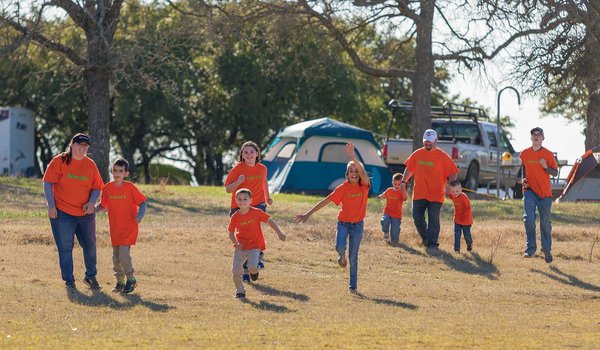 Roberto Family running down a green hill in matching orange shirts with their campsite in the background.
