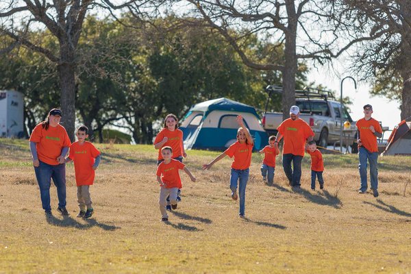 Roberto Family running down a green hill in matching orange shirts with their campsite in the background.
