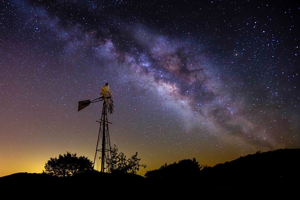 Windmill against a dark starry sky showing the Milky Way at  SKYE Texas.