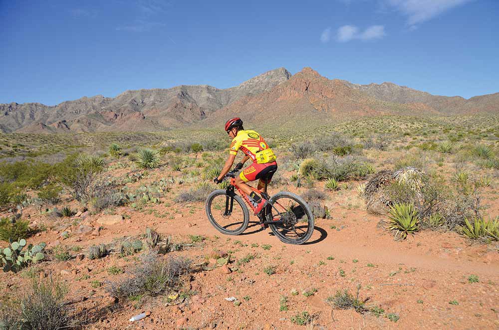 Dressed in Yellow and Red cycling gear and a red biking helmet, a cyclist rides his mountain bike along the dirt trails of Franklin Mountains state park