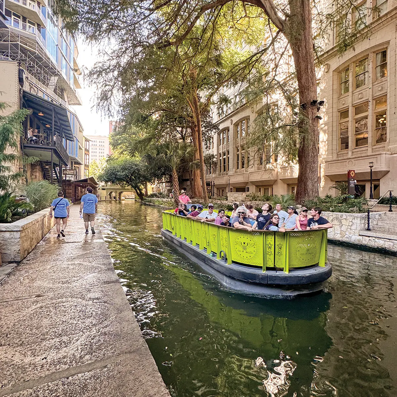 San Antonio River Walk yellowish-green boat floating the canal with buildings on either side