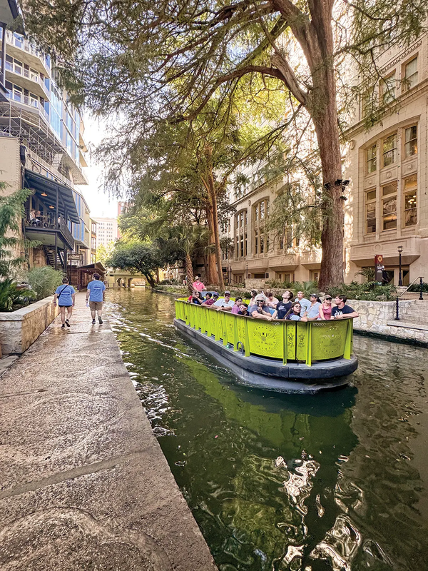 San Antonio River Walk yellowish-green boat floating the canal with buildings on either side