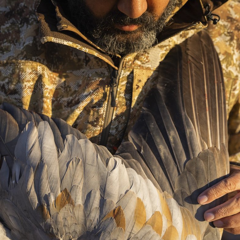 Hooded man in a camouflage coat holding a sandhill crane.