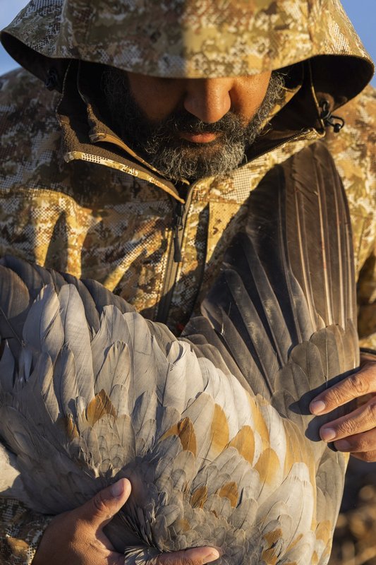 Hooded man in a camouflage coat holding a sandhill crane.