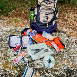 Supplies of a survival kit sitting out next to a backback