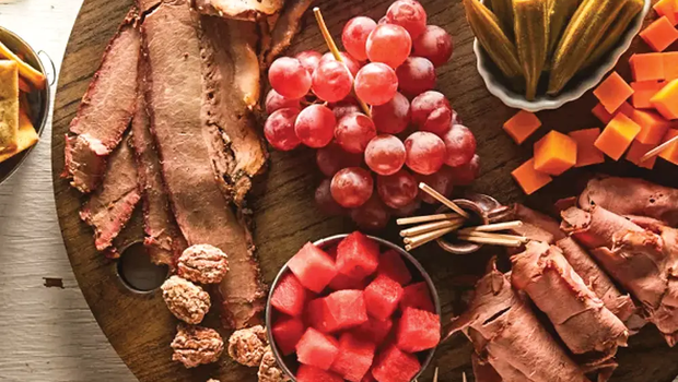 Texas Charcuterie Board containing watermelon, roast beef, brisket, cheese, and fruits on a cutting board.