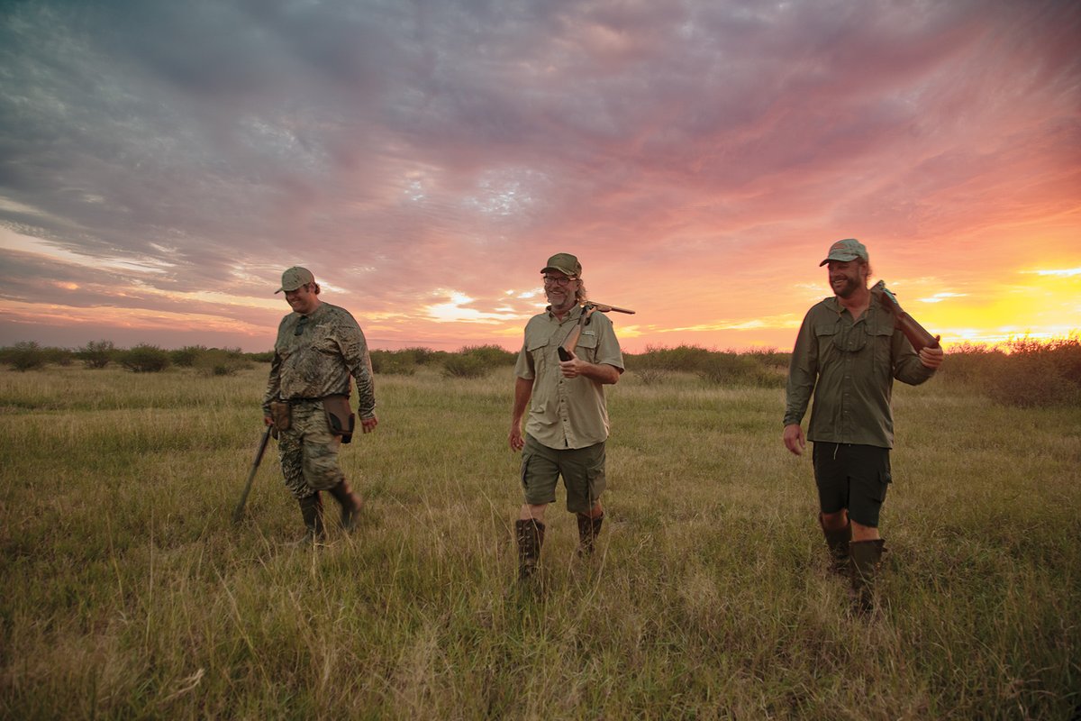 Three hunters walking through a feild at sunrise.