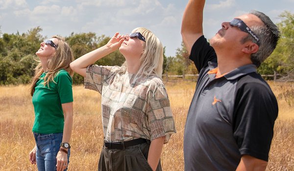 Three people looking to the sky with eclipse galsses