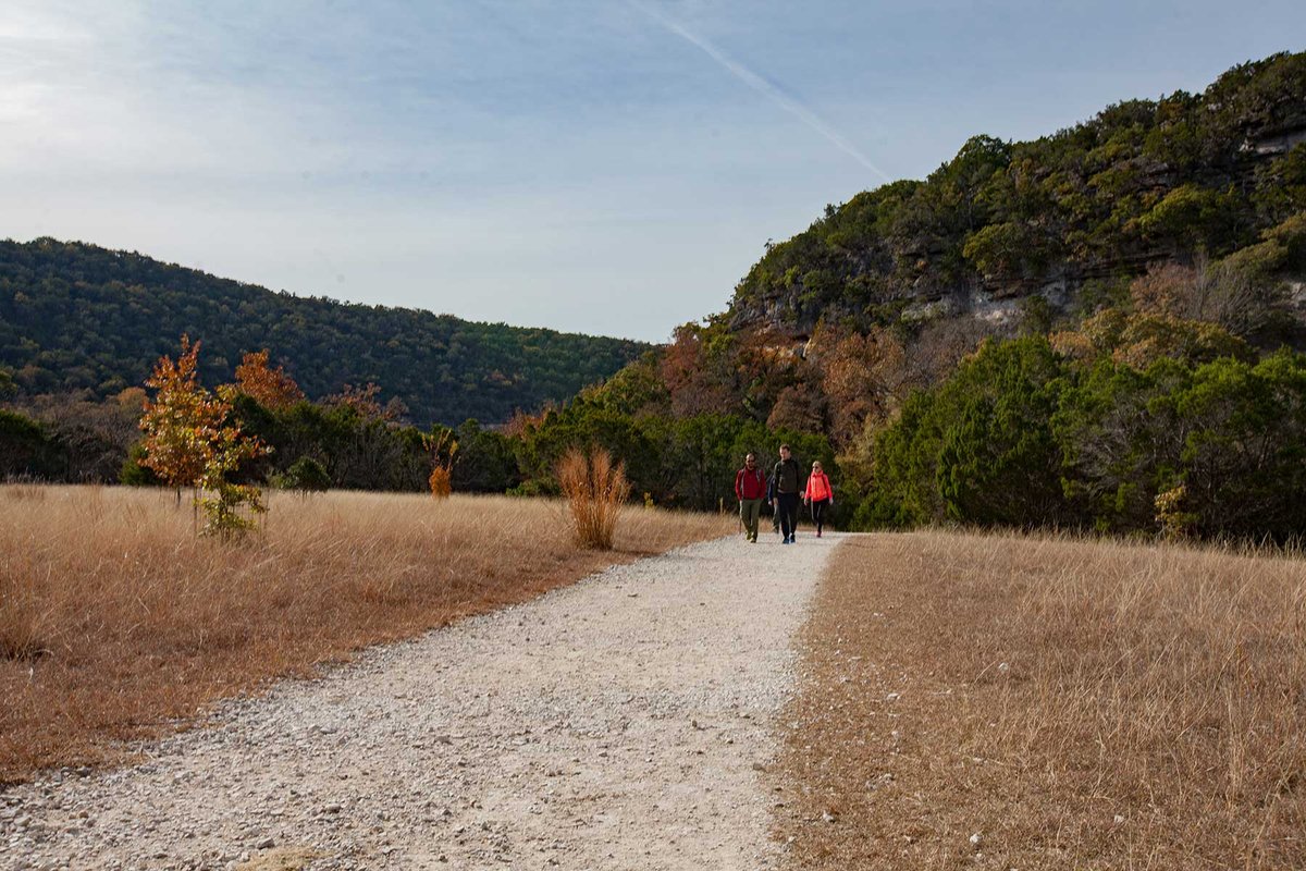 Three people walking a trail with hills in the background.