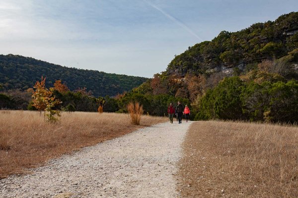 Three people walking a trail with hills in the background.
