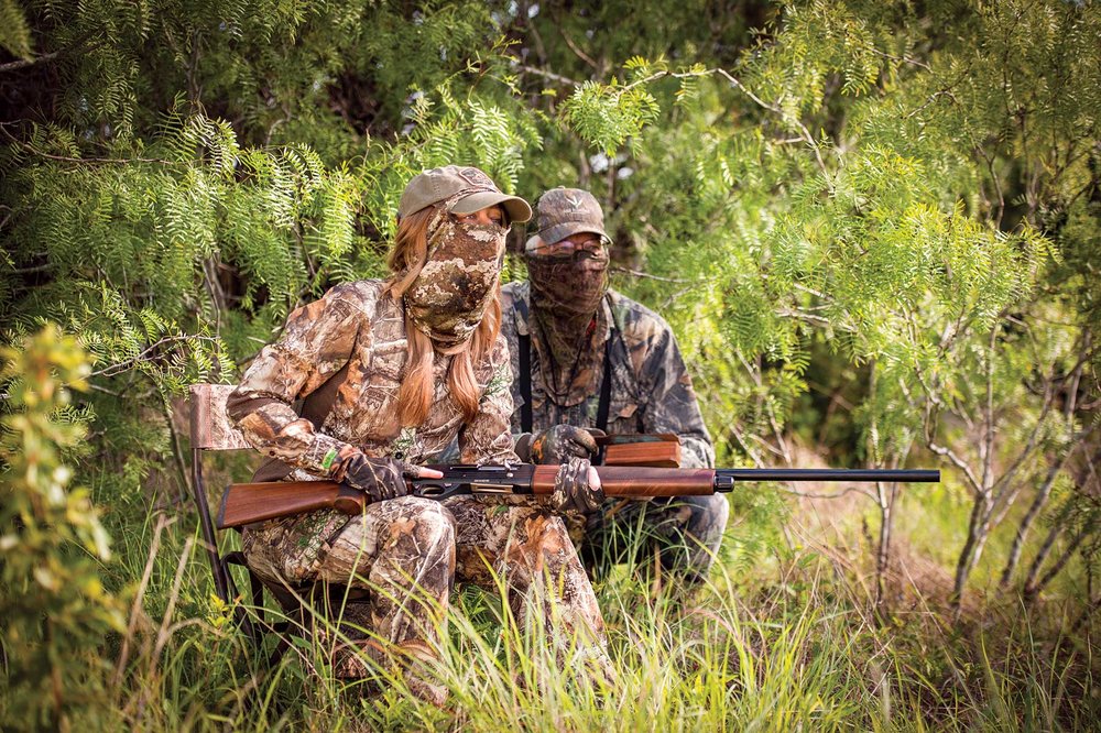 Two people in camouflage kneeling down while hunting turkey.