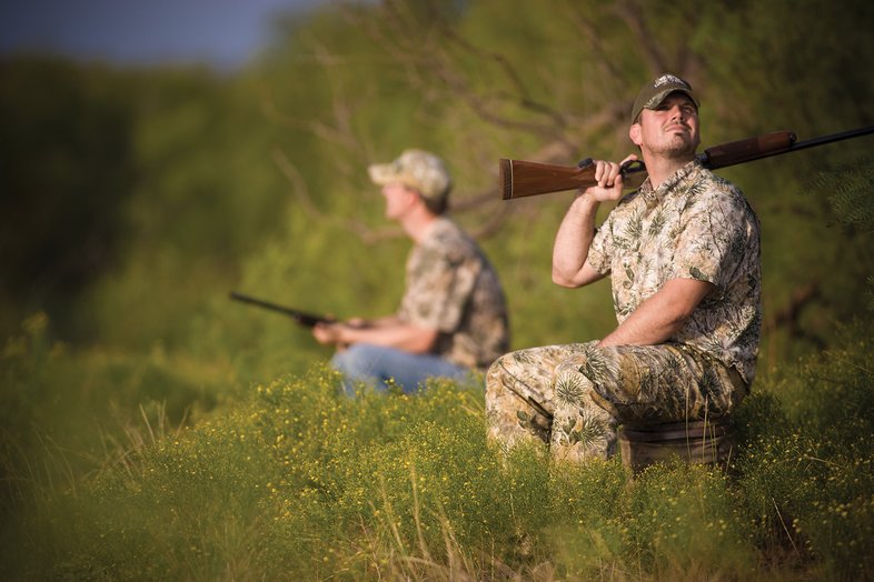 Two hunters sitting on a bench in a feild
