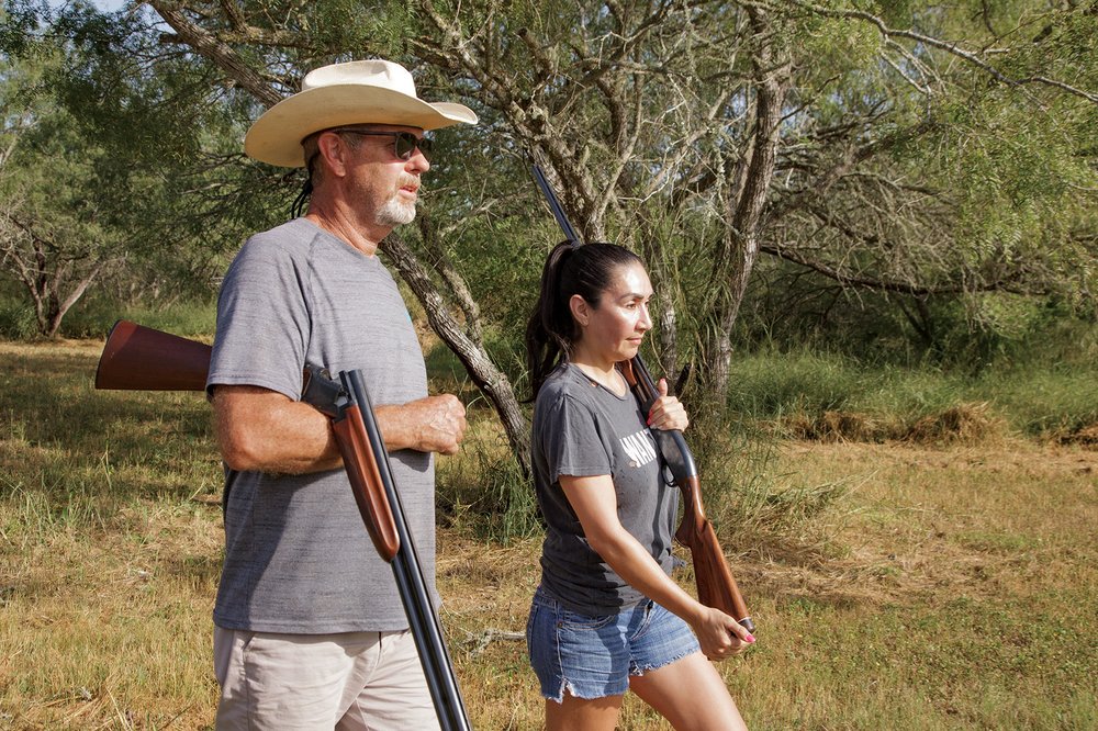 Two hunters with guns walking side by side.