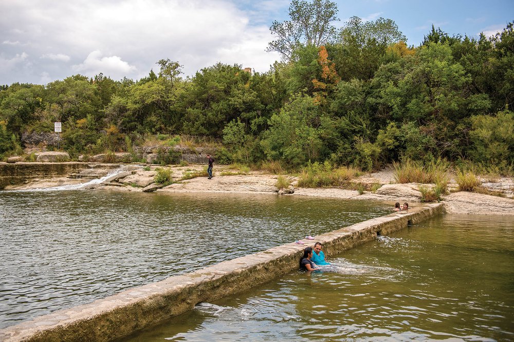 Two people sitting in the water of a springfed pool.