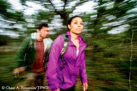 Two people walking through woods with a blurred background.
