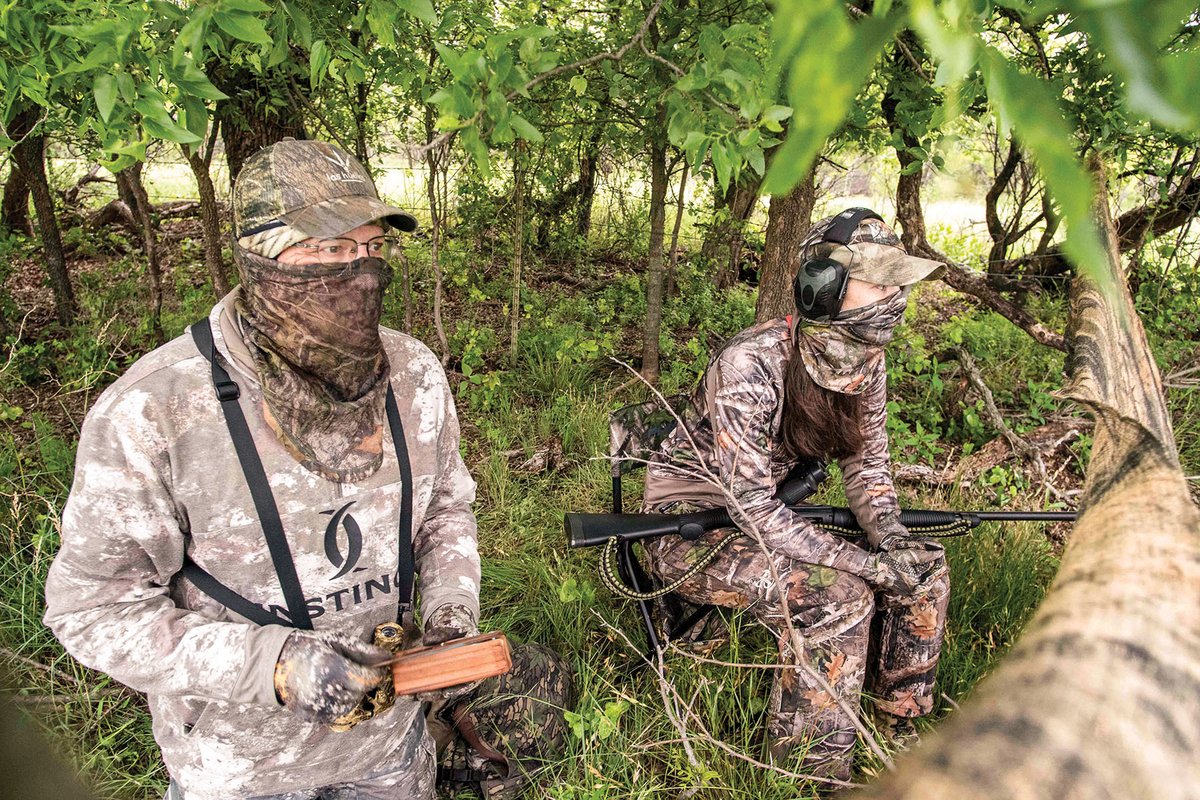 Two hunters behind a tree limb holding a turkey call.