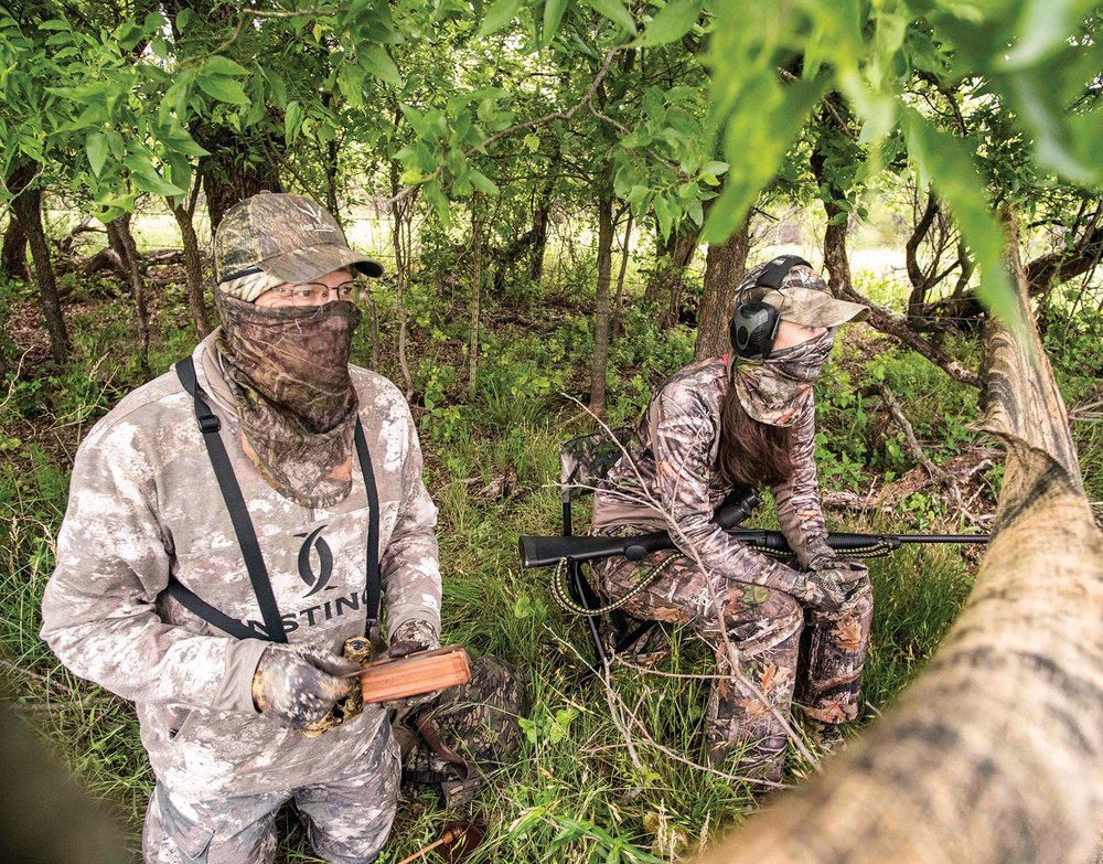 Two hunters behind a tree limb holding a turkey call.