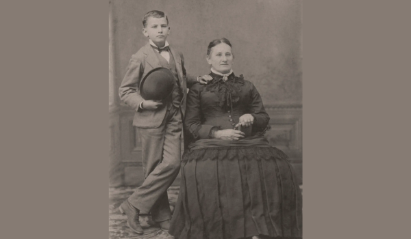 boy standing next to seated woman - black and white photo