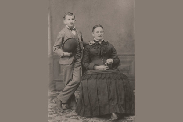 boy standing next to seated woman - black and white photo