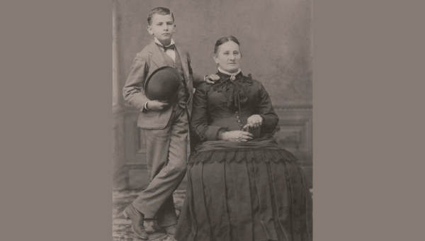 boy standing next to seated woman - black and white photo