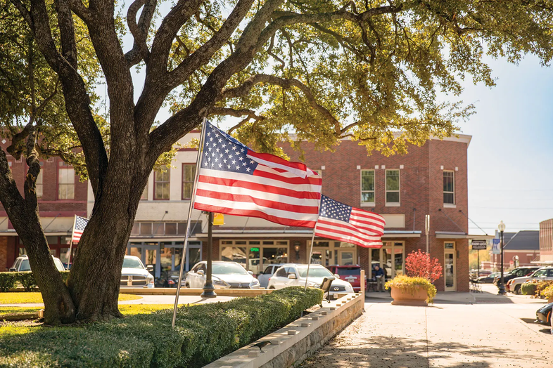 Waxahachie street with two american flag flying under a tree with storefronts in the background
