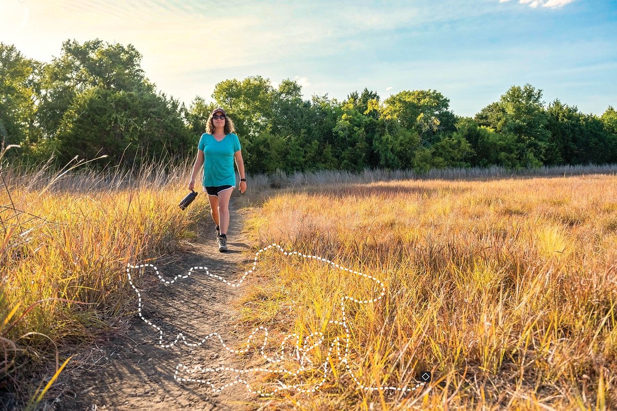 Woman walking through a field on a trail with a map of the trail.