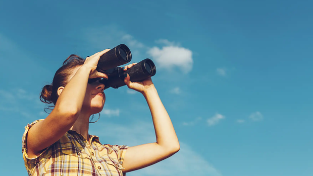 Woman looking through binoculars with a blue sky behind them