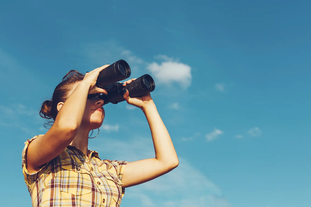 Woman looking through binoculars with a blue sky behind them