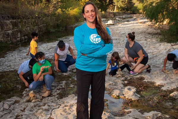 Heather Kuhlken standing in the foreground with families gathered around looking for fossils on a rocky terrain.