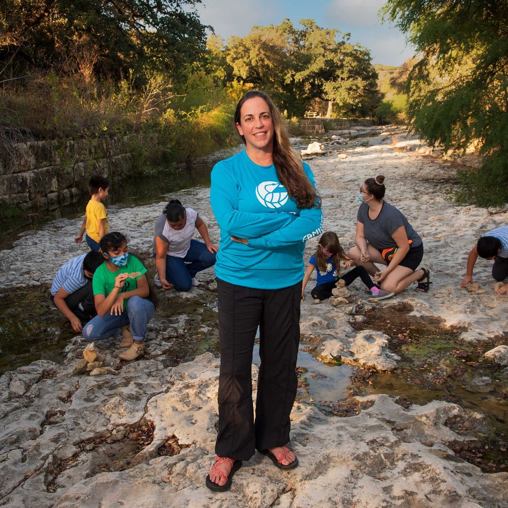 Heather Kuhlken standing in the foreground with families gathered around looking for fossils on a rocky terrain.