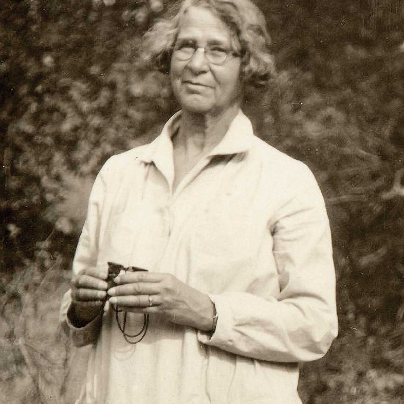 Ynes Mexia in a white dress holding binoculars